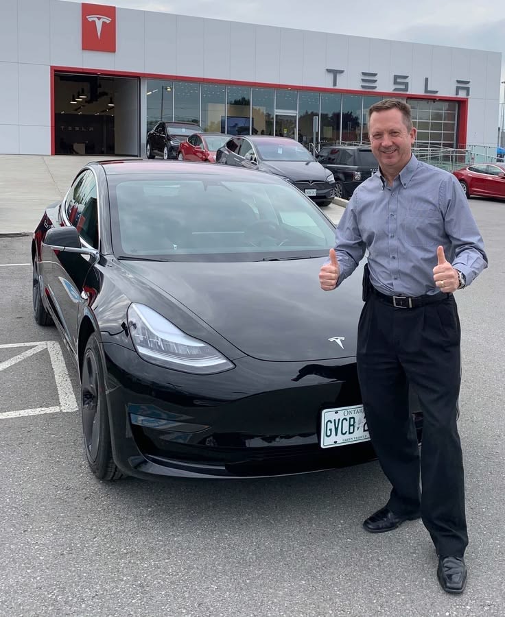 Owner standing beside a black Tesla at a delivery center
