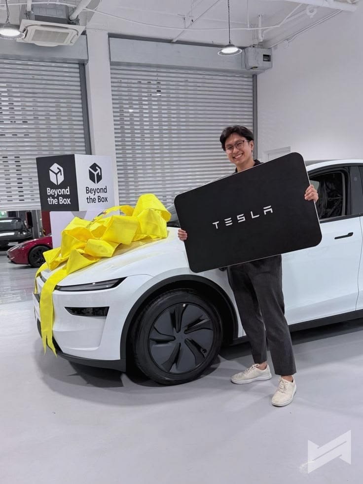 Owner holding an oversized Tesla key beside a white vehicle